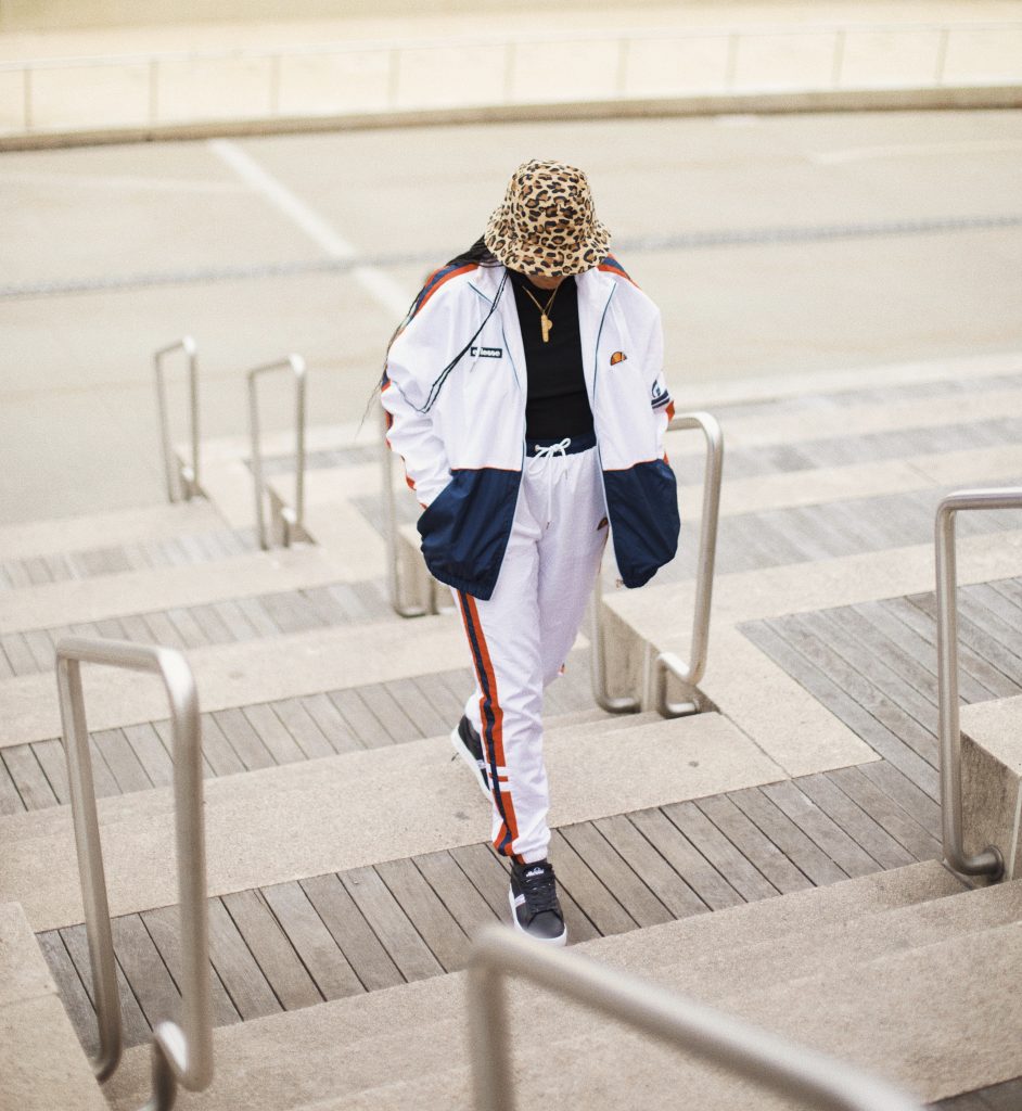How to style track pants. Dress up athlesiure outfit with blazer ellesse USA. Brooklyn New York black girl fashion style blogger blog influencer. White track suit old school ellesse leopard print bucket hat